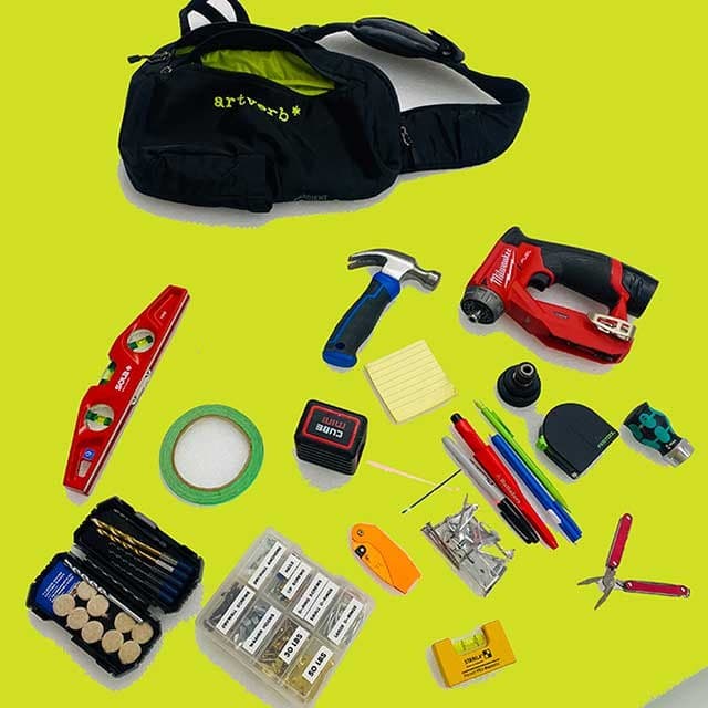 An ArtVerb tool bag with the installer's kit laid out: level, hammer, drill, tape, pencils, and hardware
