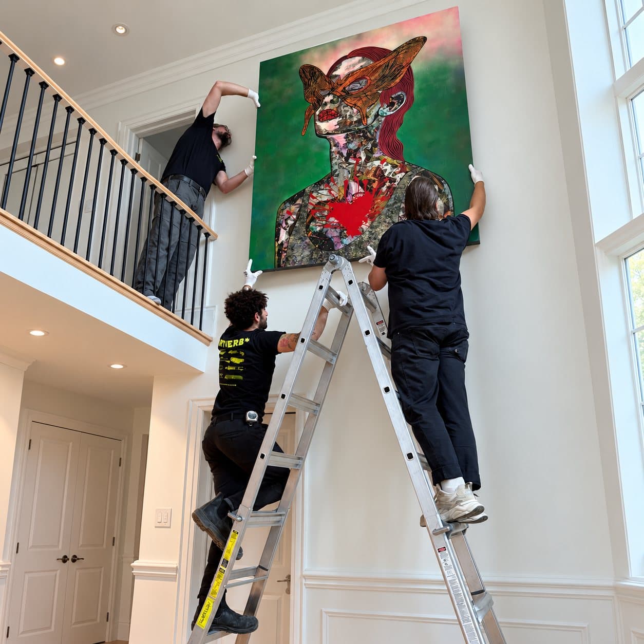 Installers on a ladder hanging a large painting in a double-height stairwell