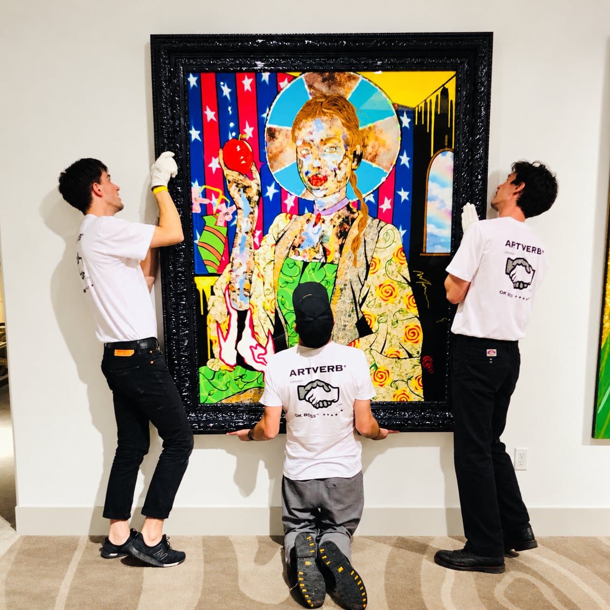 Three installers hanging a large framed painting