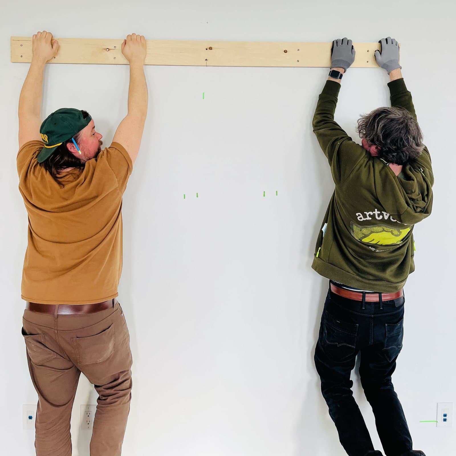 Two installers holding a timber batten level against a wall