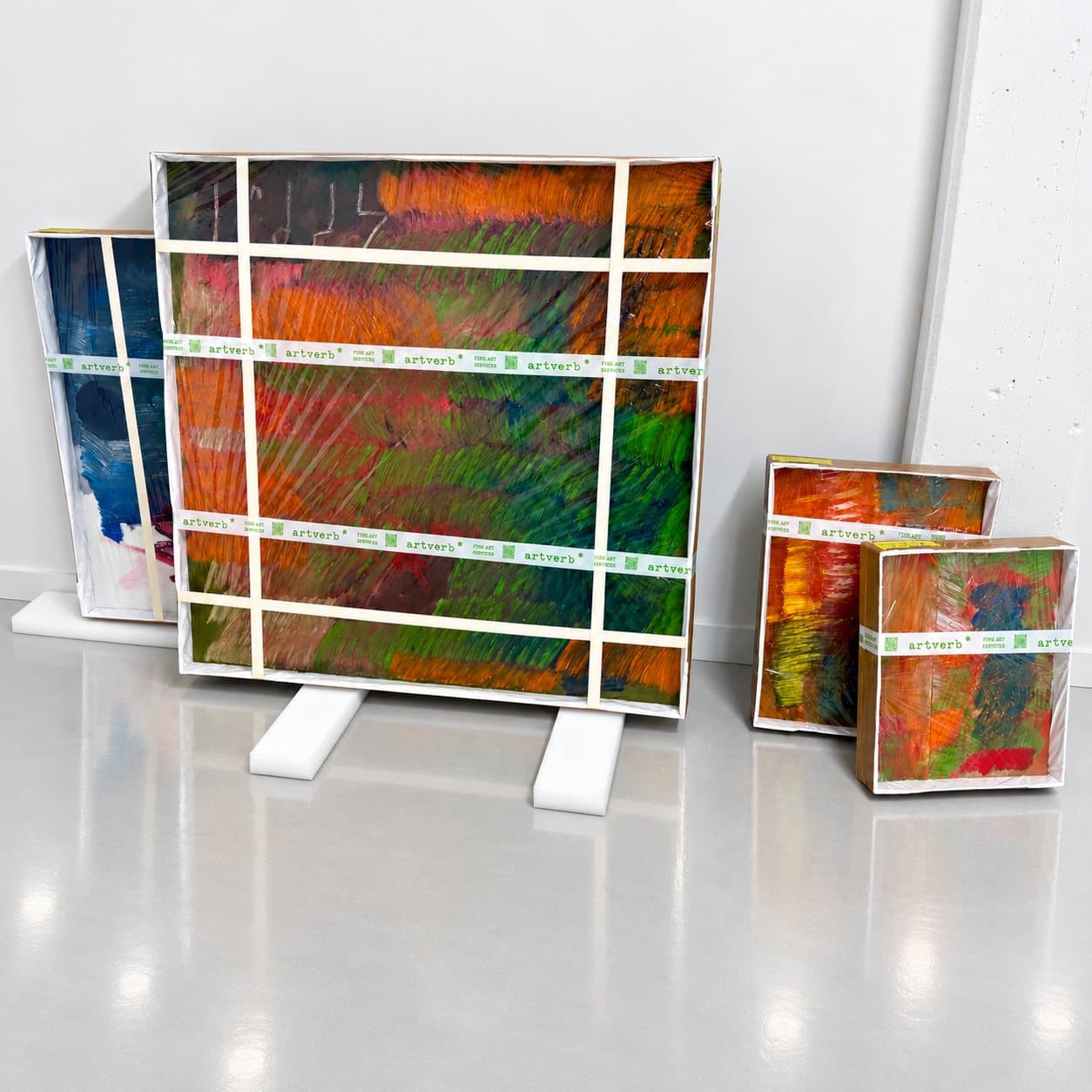 Paintings wrapped and taped with corner protection, standing on foam blocks