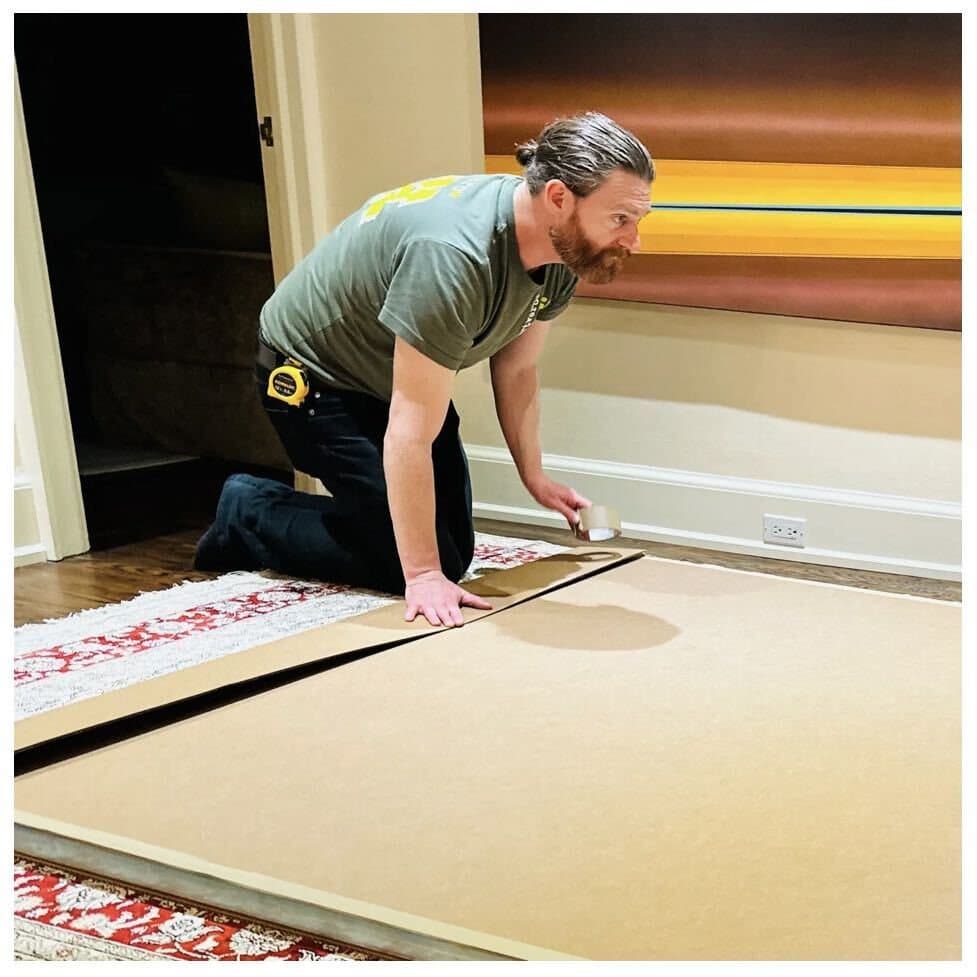 An installer unrolling protective paper over a rug before a move