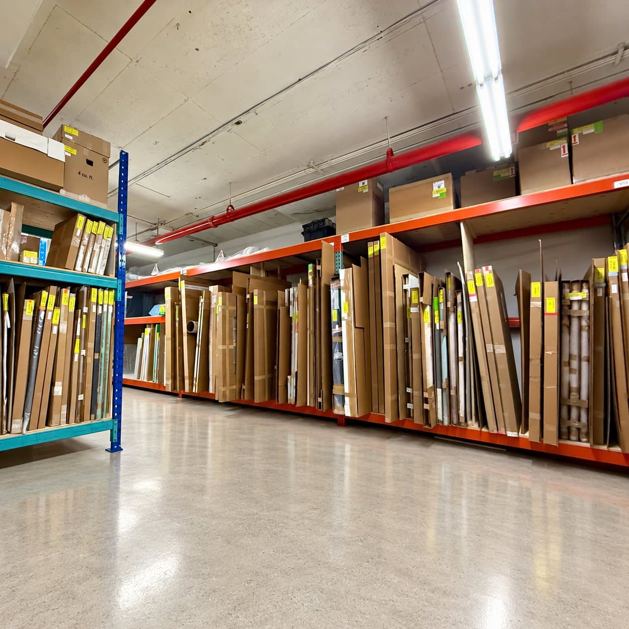 A storage aisle of racked, wrapped works under red sprinkler lines